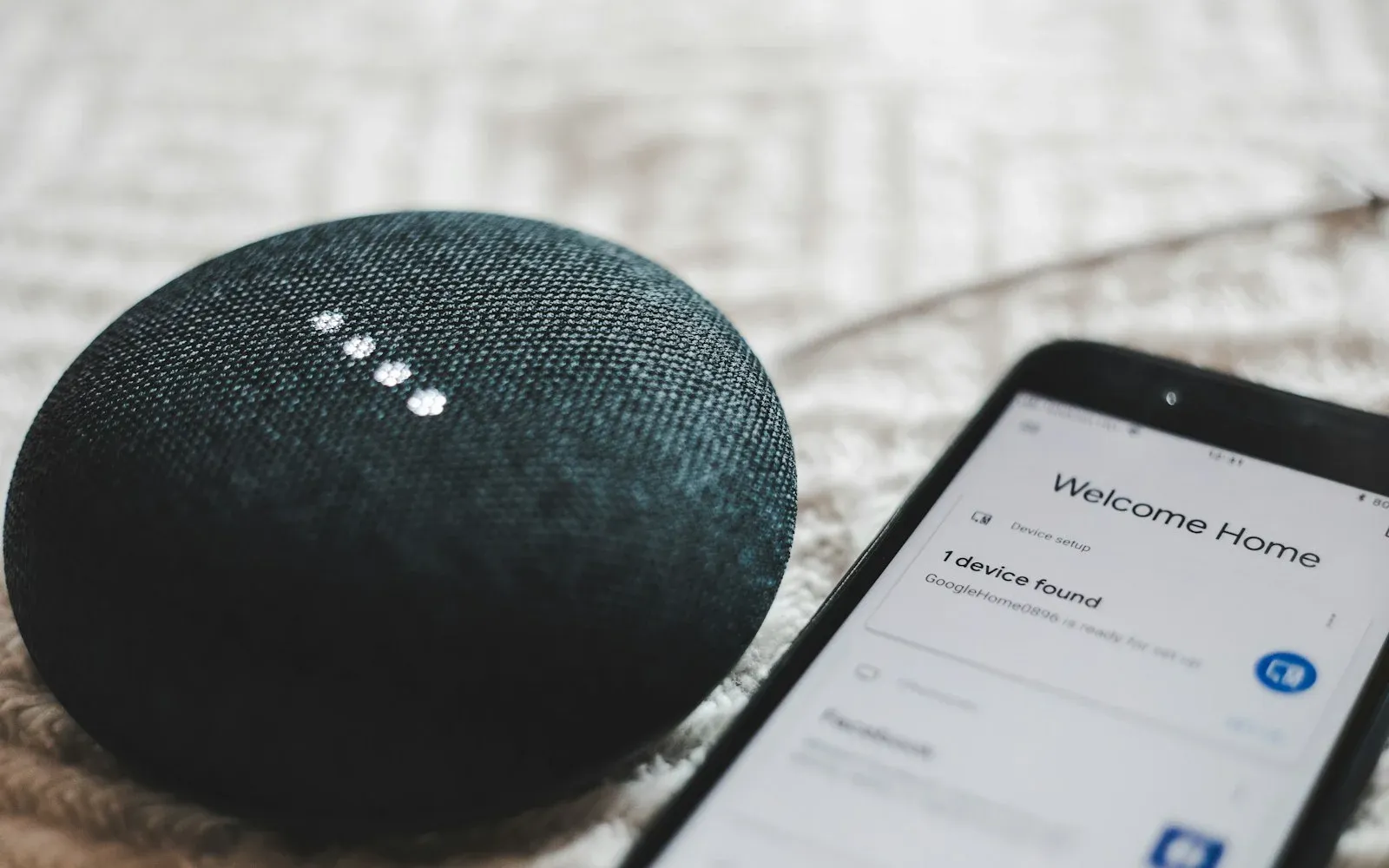 A smart speaker next to a phone showing a device setup screen