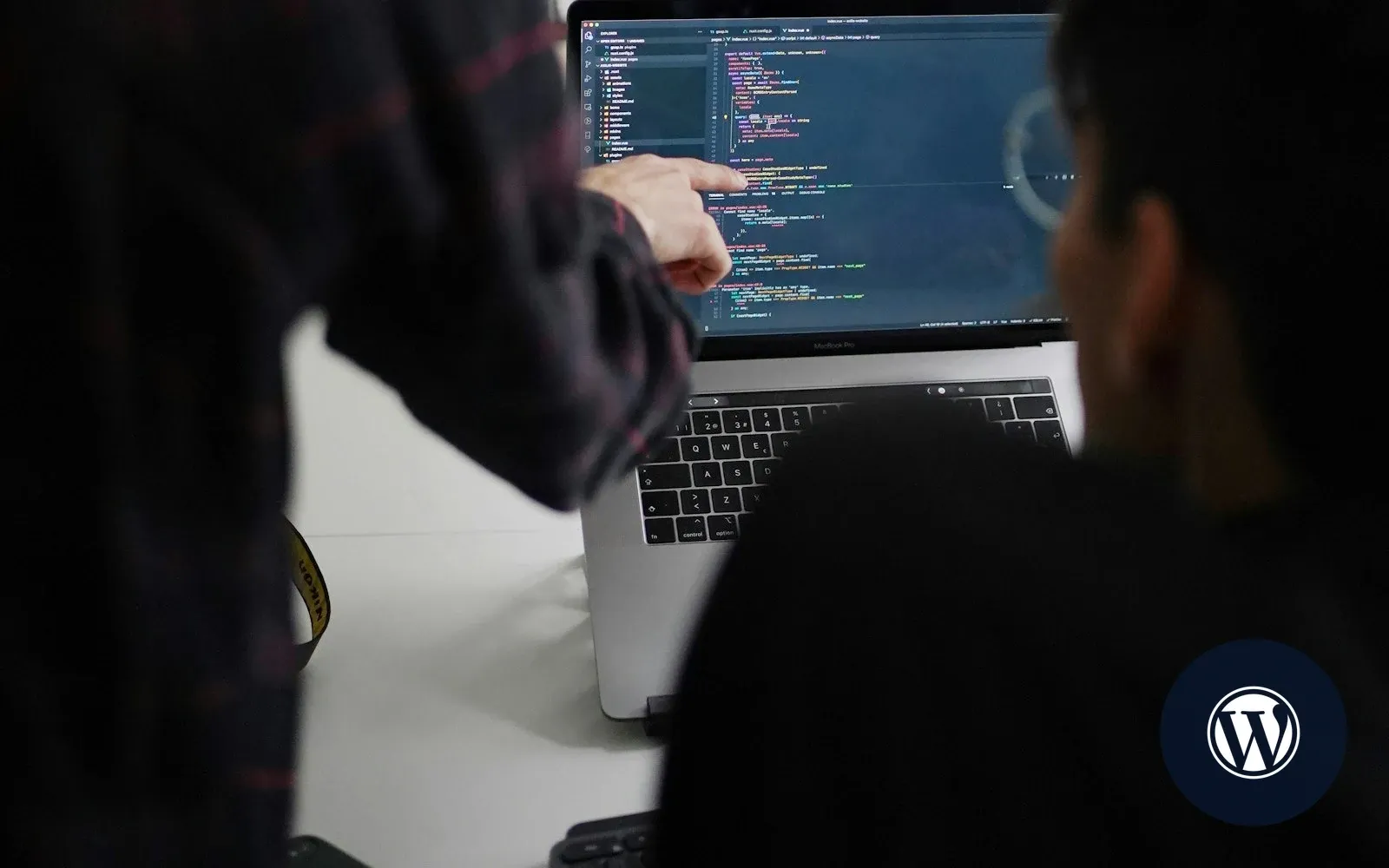 Two developers reviewing custom code on a laptop screen, with the WordPress logo marking the topic